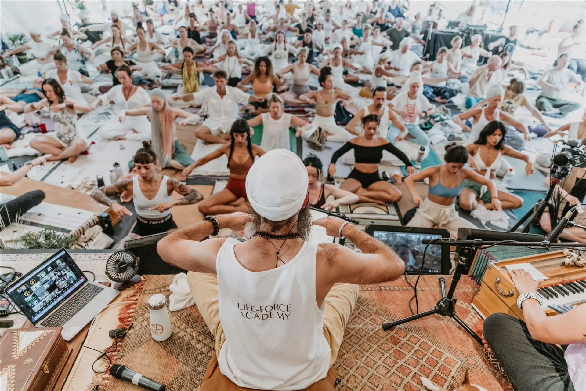 Teacher leading a large kundalini class under a sunlit tent